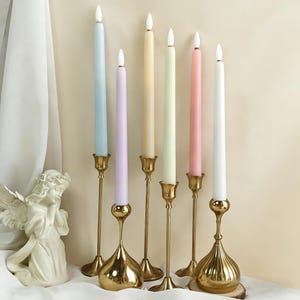 May include: Seven pastel-coloured candles in gold candle holders. The candles are in shades of blue, lilac, yellow, green, pink, and white. The candle holders have an ornate design.