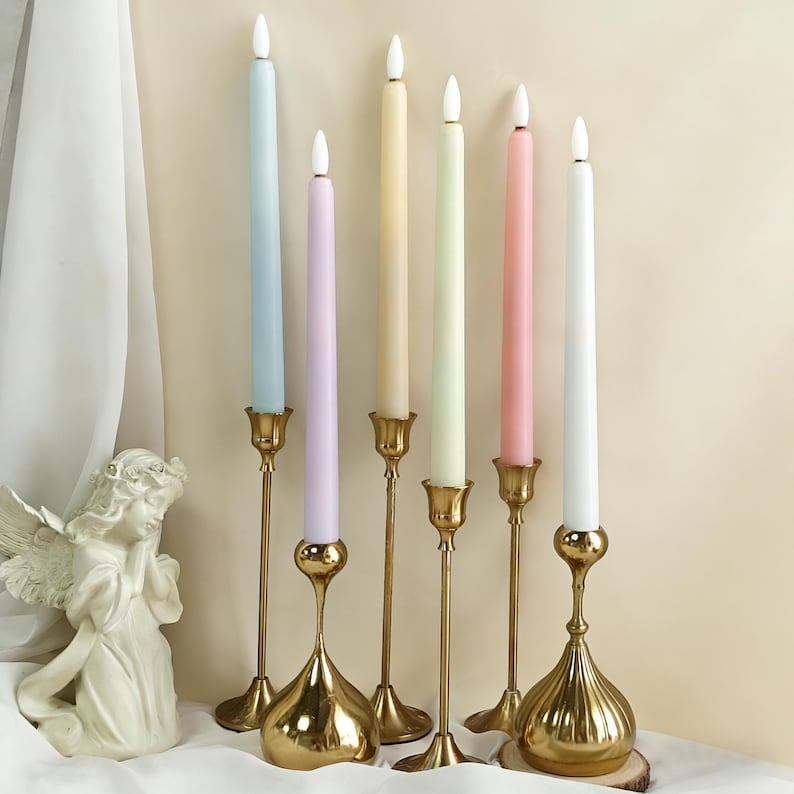 May include: Seven pastel-coloured candles in gold candle holders. The candles are in shades of blue, lilac, yellow, green, pink, and white. The candle holders have an ornate design.