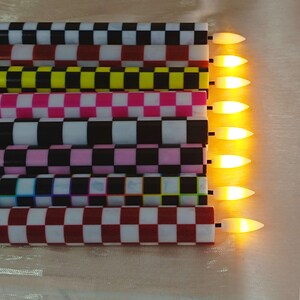 Puede incluir: Colecci&oacute;n de siete velas LED con un patr&oacute;n de cuadros en varios colores, incluyendo negro, blanco, rosa, amarillo y rojo. Las velas tienen una luz c&aacute;lida y brillante en la punta, creando un ambiente decorativo y festivo.