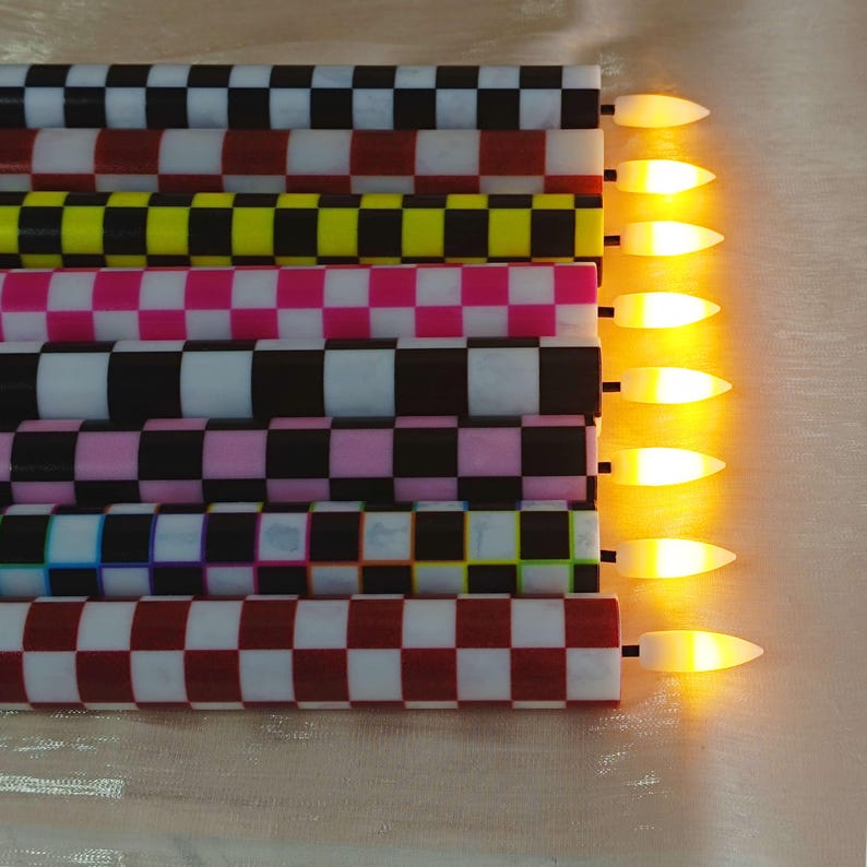 Puede incluir: Colecci&oacute;n de siete velas LED con un patr&oacute;n de cuadros en varios colores, incluyendo negro, blanco, rosa, amarillo y rojo. Las velas tienen una luz c&aacute;lida y brillante en la punta, creando un ambiente decorativo y festivo.