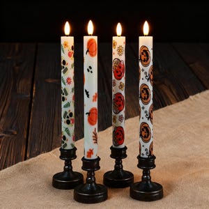 May include: Four white Halloween-themed candles with flickering LED flames. Each candle is decorated with a different pattern, including pumpkins, skulls, and floral designs. The candles are set in black metal candlestick holders, creating a festive and decorative display.