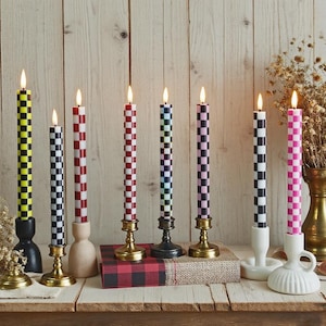 Puede incluir: Una colecci&oacute;n de velas c&oacute;nicas a cuadros encendidas en varios colores, incluyendo amarillo, rojo, negro, azul y rosa. Las velas se exhiben en diferentes candelabros sobre una superficie de madera, creando una exhibici&oacute;n decorativa y colorida.