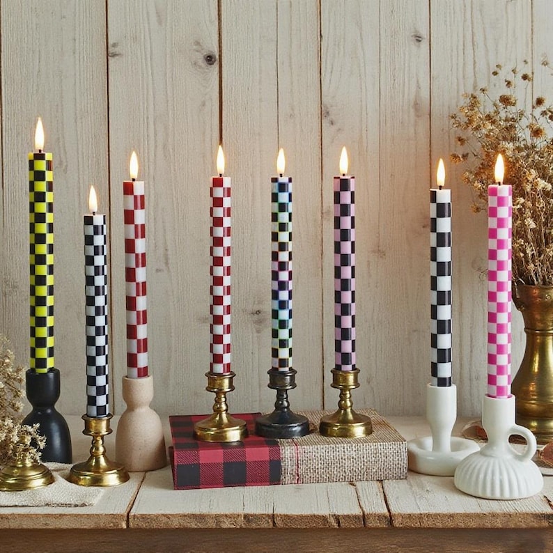 Puede incluir: Una colecci&oacute;n de velas c&oacute;nicas a cuadros encendidas en varios colores, incluyendo amarillo, rojo, negro, azul y rosa. Las velas se exhiben en diferentes candelabros sobre una superficie de madera, creando una exhibici&oacute;n decorativa y colorida.
