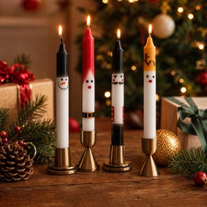 May include: Four tall taper candles standing in gold-toned metal holders. Each candle features a unique holiday design: a snowman, a Santa Claus, a nutcracker, and a reindeer. The candles are lit, with white bases and colorful painted details.