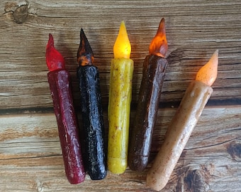 May include: Five battery-operated LED candles with a rustic woodgrain finish. The candles are in various colors, including red, black, yellow, brown, and beige.