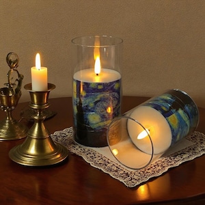 Puede incluir: Tres velas, dos en cilindros de vidrio y una en un candelabro de latón. Las velas de los cilindros presentan una impresión de "La noche estrellada" de Van Gogh. Las velas están encendidas.