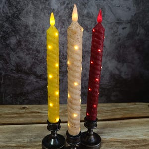 May include: Three decorative candles with a twisted design. The candles are yellow, cream, and red. The candles are lit and have a warm glow.