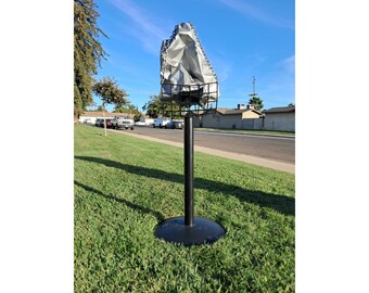 May include: A black metal stand with a gray canvas cover on top. The stand is on a grassy lawn.