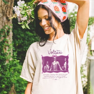 May include: A white t-shirt with a purple graphic of three people in a framed image. The graphic includes the text "team Volturi" and a quote: "Don't bother. I think you know who we are, and you must know that there is no point in trying to surprise us. Or hide from us. Or fight us. Or run."