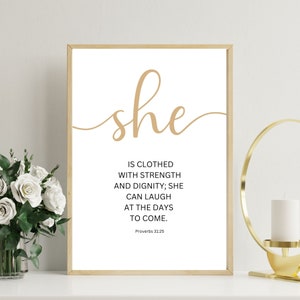 May include: A framed print with a white background and gold text. The text reads "she is clothed with strength and dignity; she can laugh at the days to come. Proverbs 31:25".