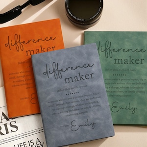 May include: Three leather-bound journals with the word "difference maker" and a definition of the word. The journals are in blue, green, and orange. The name "Emily" is written on the blue and green journals.
