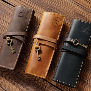 May include: Three leather pen cases in brown, tan, and black, each secured with a leather strap and a decorative key. The brown case has the letter "D" and the name "Richard" engraved. The tan case has the letter "H" and the black case has the letter "K" and the name "KING" engraved.