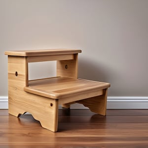 Op de afbeelding: Een houten krukje met twee treden en een natuurlijke afwerking. De kruk heeft een rechthoekige bovenste trede en een lagere trede, verbonden door zijsteunen. De houtnerf is zichtbaar en de kruk is ontworpen met afgeronde randen.