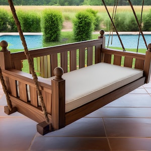May include: A wooden swing bench with a white cushion, hanging from ropes. The swing is on a patio with a pool in the background.