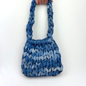 Può includere: Una borsa tote in denim blu con un manico intrecciato. La borsa è realizzata in denim riciclato e ha un aspetto unico e testurizzato.