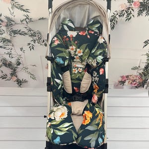 May include: A stroller seat liner with a floral pattern in shades of green, white, orange, and pink. The liner has a headrest and a padded seat.
