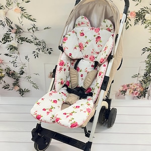 May include: A white stroller with a floral patterned seat and headrest. The stroller has a black frame and wheels.