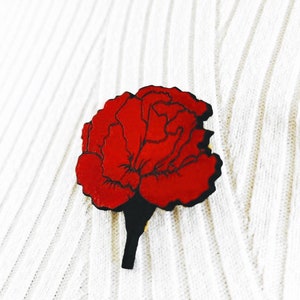 May include: A red carnation flower pin on a white knitted fabric background.