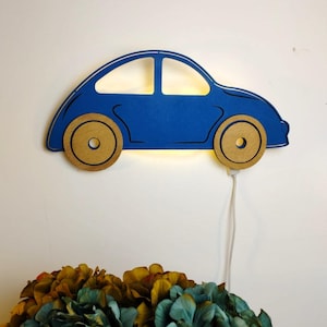 Puede incluir: Una luz nocturna de madera en forma de coche azul con un cable blanco. El coche tiene una luz amarilla en el interior y ruedas de madera.