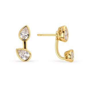 May include: A pair of gold stud earrings featuring a double pear-shaped design. Each earring consists of two clear, faceted pear-cut stones set in gold, connected by a curved gold bar, with a post back for secure attachment to the earlobe.