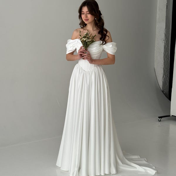 Vestido de novia con corsé, cintura vasca y mangas drapeadas con hombros descubiertos
