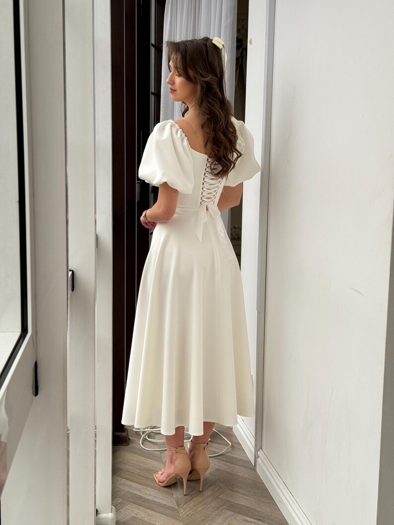 May include: A white midi dress with a lace-up back and puff sleeves.