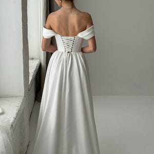 May include: A white off-the-shoulder wedding dress with a lace-up back.