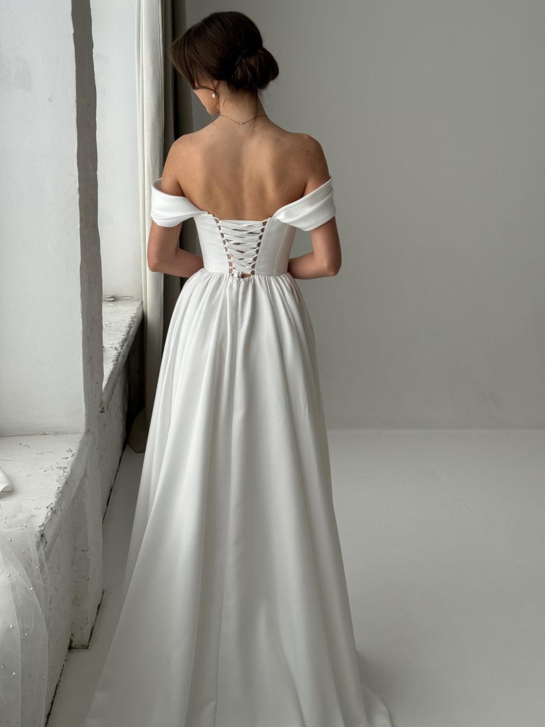 May include: A white off-the-shoulder wedding dress with a lace-up back.