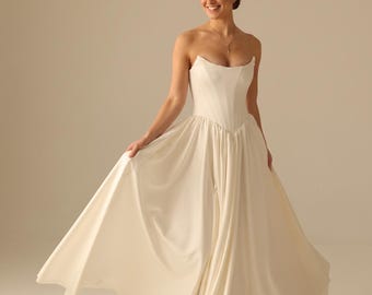 May include: A floor-length ivory strapless gown featuring a structured corset-style bodice with a pointed waistline and a full, flowing skirt made of smooth fabric. The dress has a clean, minimalist design with a subtle sheen and a flared silhouette.