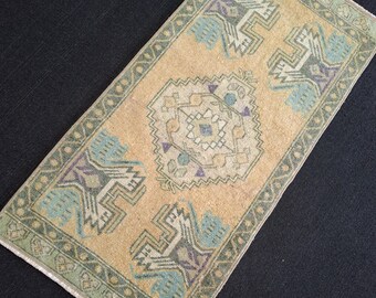 Puede incluir: Una alfombra rectangular de estilo vintage con un diseño de medallón central. La alfombra presenta un fondo beige con patrones geométricos en tonos de azul, verde y morado. El borde es de un verde más oscuro, y la alfombra parece estar hecha de material tejido.