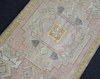 May include: A rectangular, vintage-style rug with a faded, geometric pattern. The rug features a soft pink field with accents of beige, gray, and yellow. The edges are bordered with a yellow-green trim, creating a warm, inviting aesthetic.