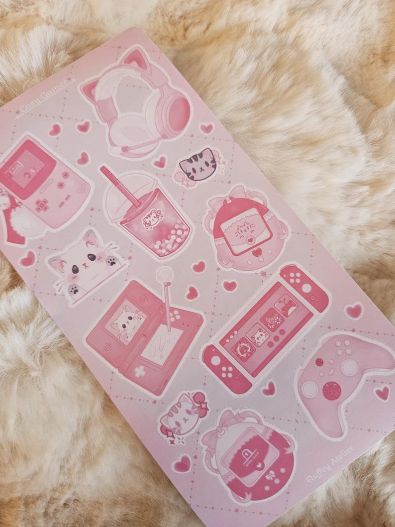 May include: Pink and white sticker sheet with a variety of cute gamer-themed illustrations, including a cat wearing headphones, a game console, a boba tea, and a cat holding a game controller. The sheet also includes hearts, stars, and other decorative elements. The text "Sluggy Atelier" is in the bottom right corner.