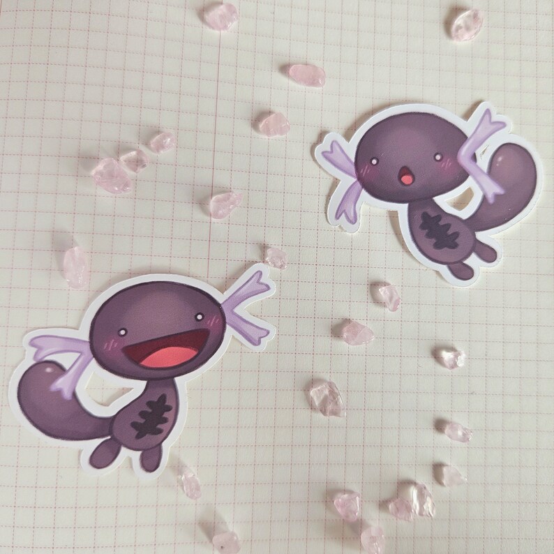May include: Two purple axolotl stickers with white outlines and pink accents. The axolotls are smiling with their mouths open and have small, black eyes. They are both in a cartoon style.