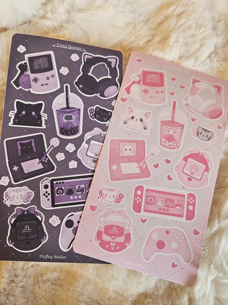 May include: Two sheets of stickers featuring a pink and a gray color scheme. The stickers feature various cute illustrations of cats, game consoles, and other gaming-related items. The text "Cozy Gamer" and "Fluffy Atelier" is printed on the sheets.