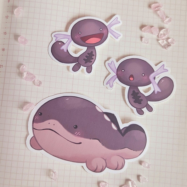 May include: Three cartoon stickers featuring axolotls. The stickers are on a white gridded background. The axolotls are purple, pink, and gray with white spots. The axolotls have big eyes and smiles.
