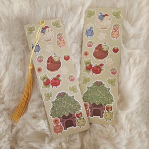 Peut inclure: Deux marque-pages rectangulaires avec des illustrations fantaisistes de poulets, de fraises et de maisons aux toits feuillus. Les marque-pages ont un fond beige clair et une gland doré. Les illustrations sont en rouge, marron, vert et jaune.