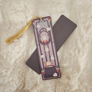 以下が含まれることがあります： 紫と金の幽霊と釜が描かれたしおり。しおりには金色の房がついています。