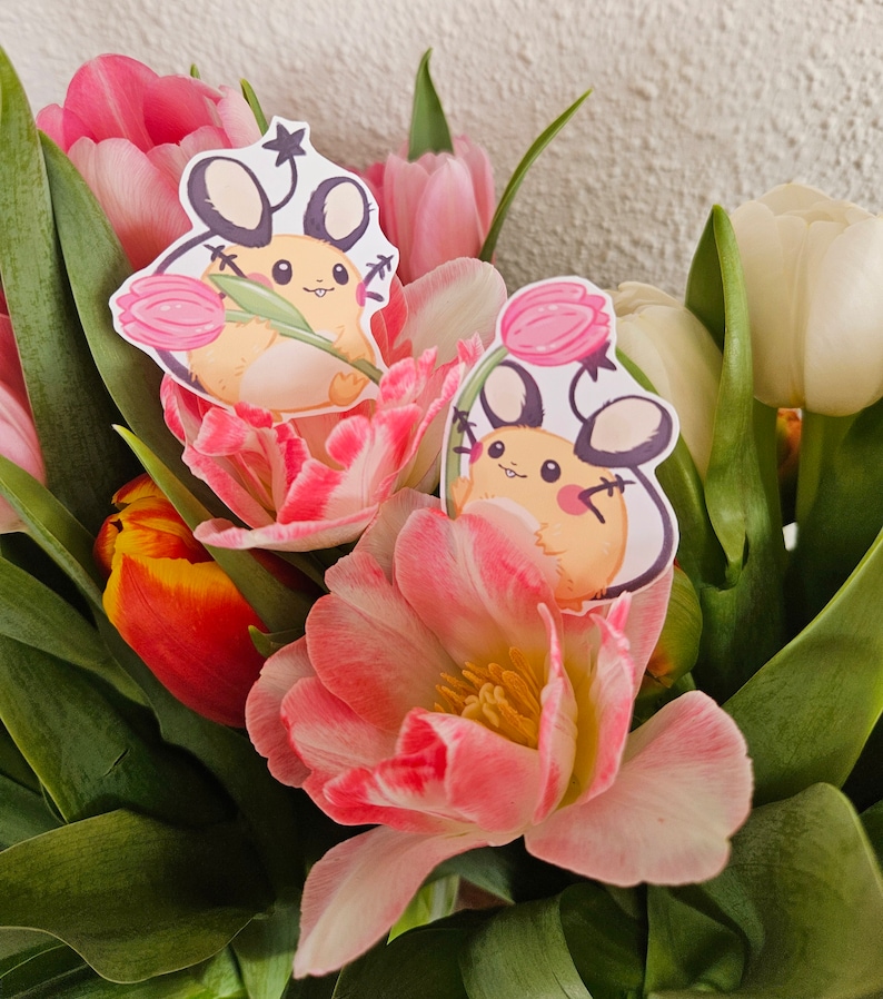 May include: Two pink and white tulips with cartoon stickers of a small, yellow, mouse-like creature holding a pink flower. The stickers are on the tulips.