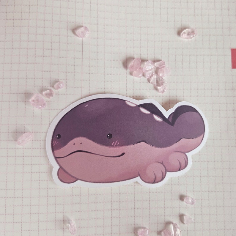 May include: A sticker of a cartoon purple and pink creature with a wide, flat body and small legs. The creature has a friendly expression and is lying on its belly.