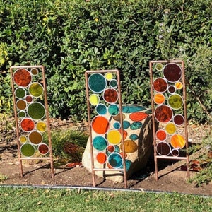 May include: Three copper metal garden stakes with colorful glass circles. The circles are in shades of red, orange, yellow, green, and blue.