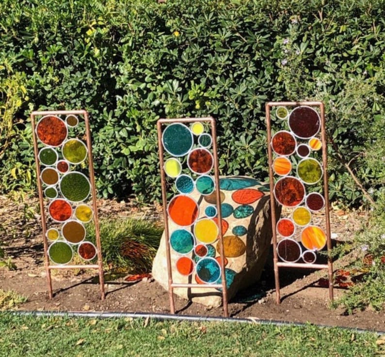 May include: Three copper metal garden stakes with colorful glass circles. The circles are in shades of red, orange, yellow, green, and blue.