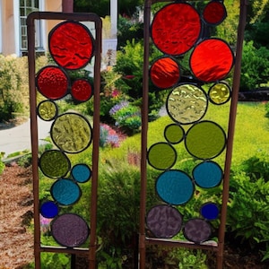 Puede incluir: Dos estacas de jard&iacute;n de metal altas con c&iacute;rculos de vidrio coloreado. Los c&iacute;rculos son en tonos de rojo, verde, azul y morado. Las estacas est&aacute;n colocadas en un jard&iacute;n.