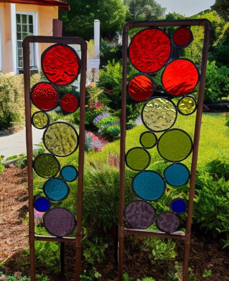 Puede incluir: Dos estacas de jard&iacute;n de metal altas con c&iacute;rculos de vidrio coloreado. Los c&iacute;rculos son en tonos de rojo, verde, azul y morado. Las estacas est&aacute;n colocadas en un jard&iacute;n.
