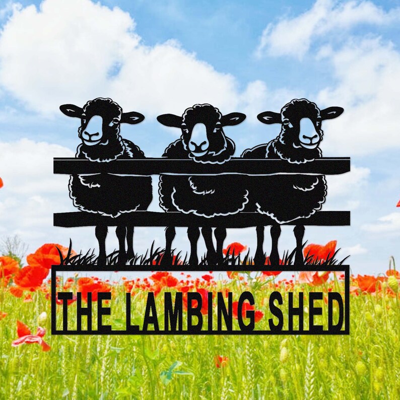 May include: Black metal sign featuring three sheep peering over a fence. The sign includes the text "THE LAMBING SHED" in a rectangular frame, set against a backdrop of a field of red poppies and a blue sky with clouds.