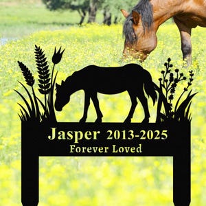 Könnte beinhalten: Schwarze Metallsilhouette eines Pferdes mit Gras und Blumen. Das Schild trägt die Aufschrift "Jasper 2013-2025 Forever Loved".