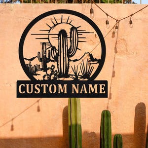 May include: Black metal silhouette of a desert scene with a sun, mountains, and cacti. The text "CUSTOM NAME" is below the scene.