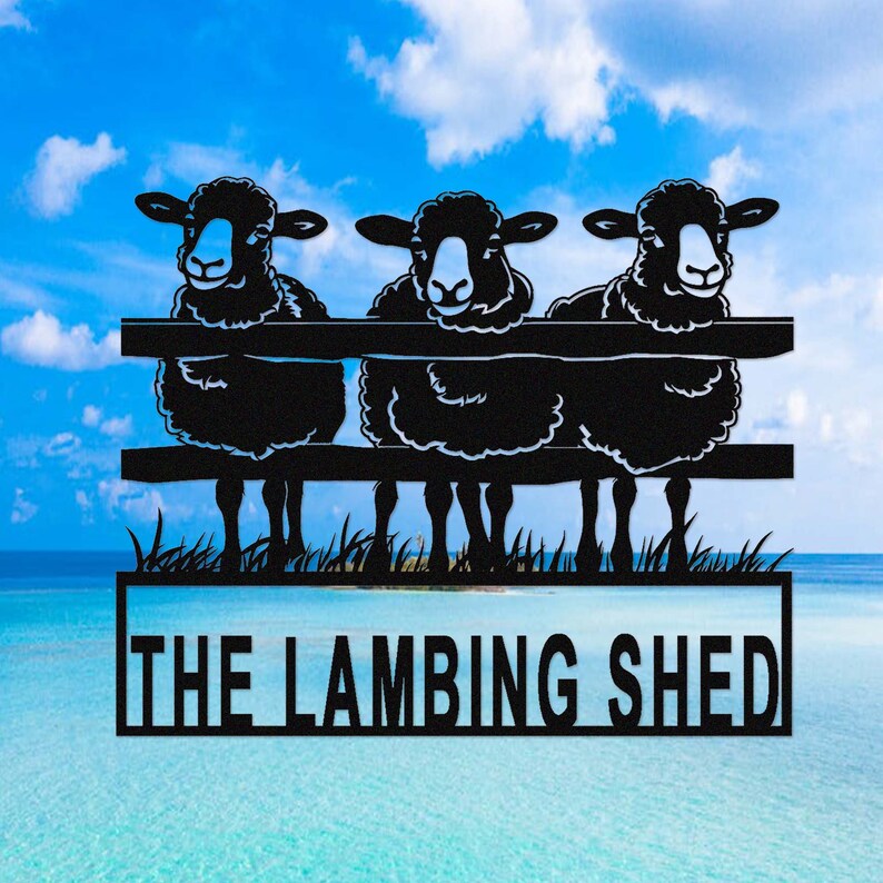 May include: Black metal sign featuring three sheep peering over a fence. The sign includes the text "THE LAMBING SHED" in a rectangular frame. The background shows a blue sky and ocean.