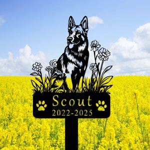 May include: Black metal silhouette of a German Shepherd dog sitting in a bed of flowers with a sign that reads "Scout 2022-2025" and paw prints.