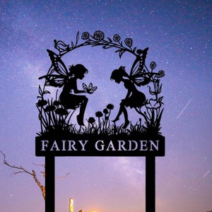 May include: Black metal silhouette of two fairies with wings, sitting on a bed of flowers, with the text "Fairy Garden" on a sign below. The silhouette is set against a starry night sky.