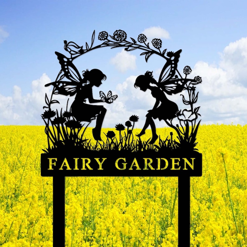 May include: Black metal silhouette of two fairies with wings, sitting on a flower bed with a butterfly, under a floral arch. The sign reads "FAIRY GARDEN".